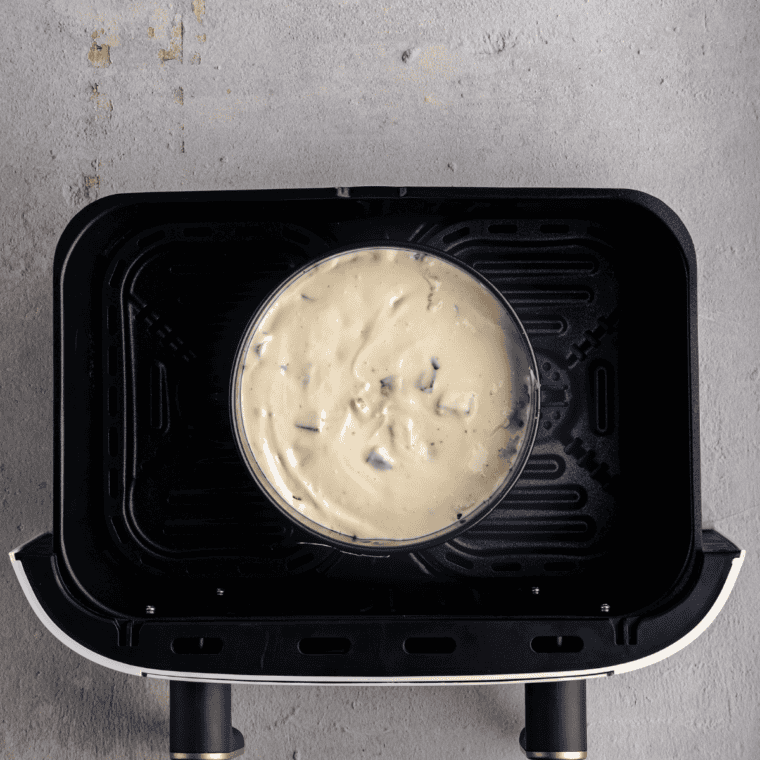 Snickers cheesecake in a springform pan inside the air fryer basket before baking at 300°F