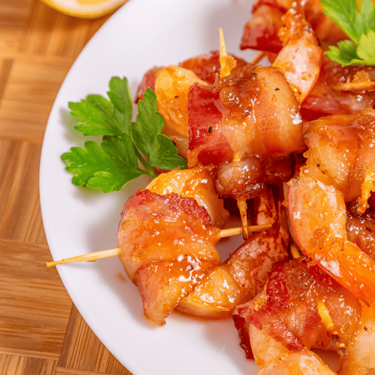 Bacon wrapped shrimp stuffed with cream cheese and jalapeño arranged on a platter with dipping sauce