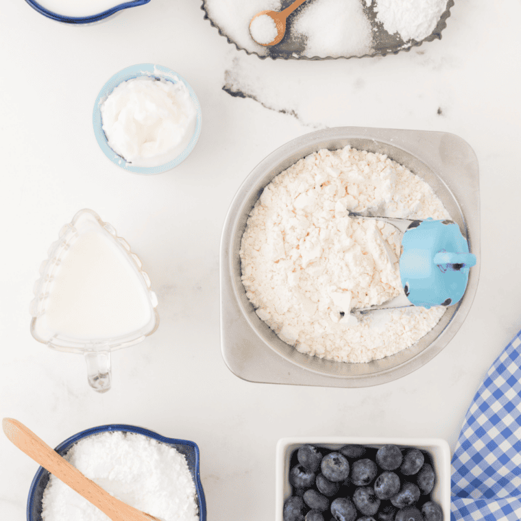 panera blueberry scones recipe ingredients on kitchen table with flour, cold butter, fresh blueberries, and heavy cream