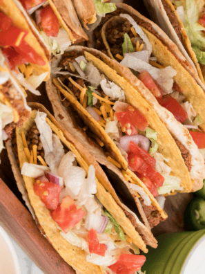 Three crispy Del Taco copycat beef tacos topped with shredded cheddar and lettuce on a plate