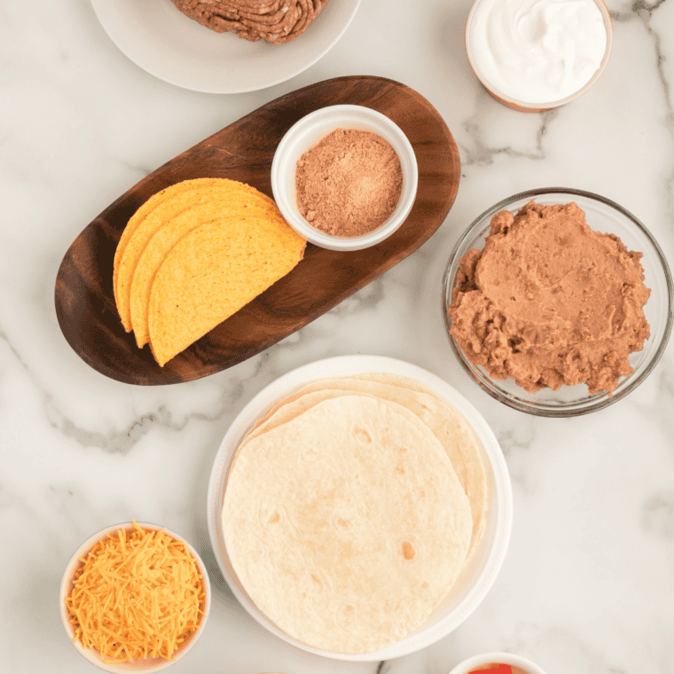 Ingredients for Del Taco copycat beef tacos laid out: ground beef, taco shells, cheddar, lettuce, and spices