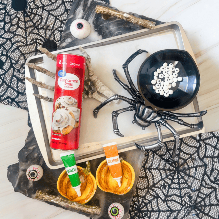 Ingredients for easy Halloween cinnamon rolls including canned dough, orange and green food coloring, and candy eyes.