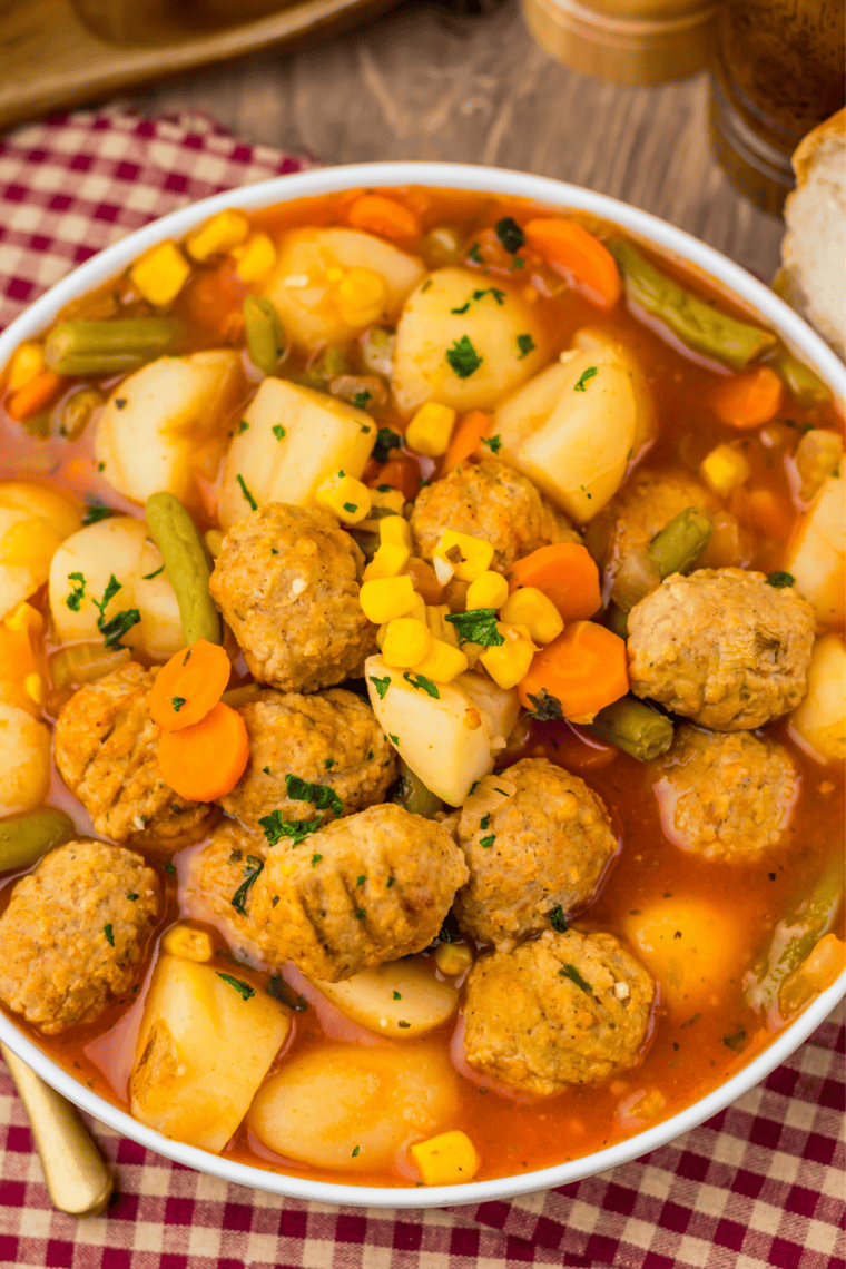 A white ceramic bowl of slow cooker meatball vegetable soup served with a spoon on a wooden table