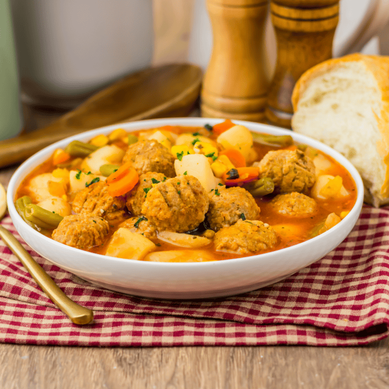 Bowl of slow cooker meatball vegetable soup with potatoes, carrots, and green beans, topped with fresh parsley
