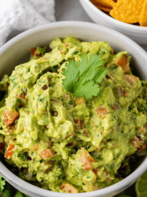 Bowl of fresh vegan guacamole topped with cilantro and pepitas, with a tortilla chip scooping a bite