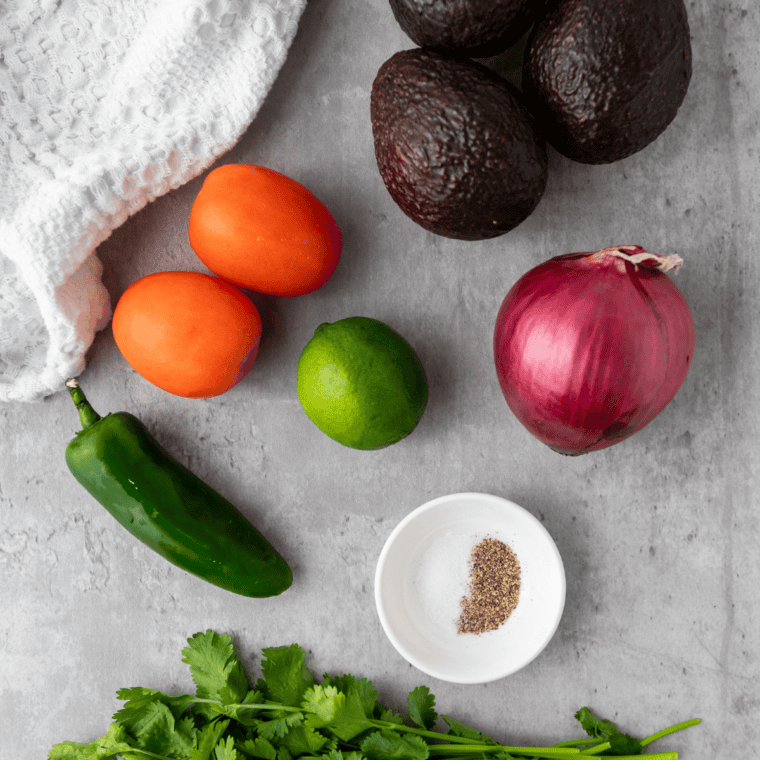 Ingredients for vegan guacamole recipe laid out: ripe Hass avocados, lime, white onion, jalapeño, cilantro, garlic, and salt