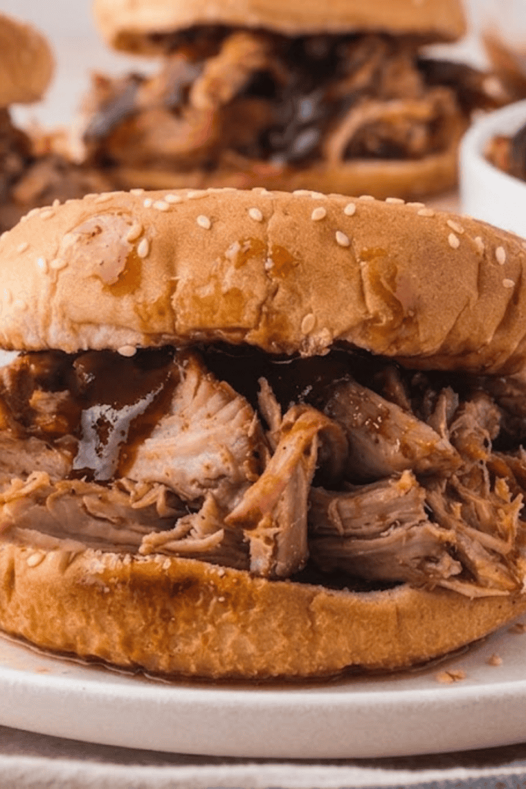 Close-up of a pulled pork sandwich showing tender saucy meat and creamy slaw on a toasted bun