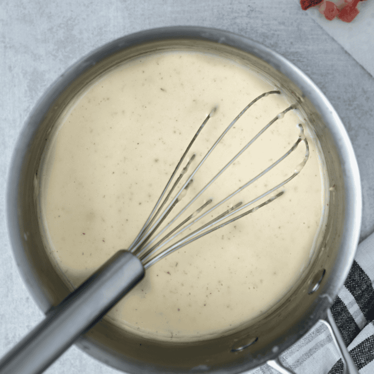 Whisking milk and cream into a smooth cheese sauce base