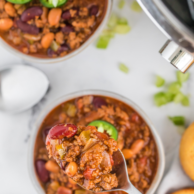 Homemade mild chili seasoning blend in a glass spice jar with mixed spices on a wooden surface.
