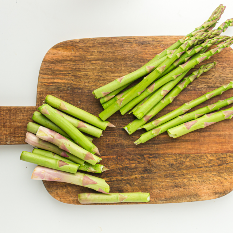Trimming the woody ends off fresh asparagus spears on a cutting board.