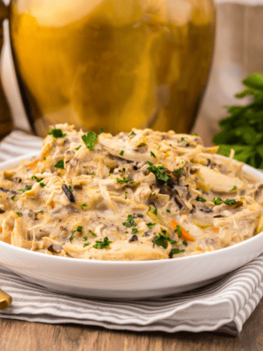 Bowl of creamy slow cooker chicken and wild rice soup with carrots and celery, garnished and served with crusty bread