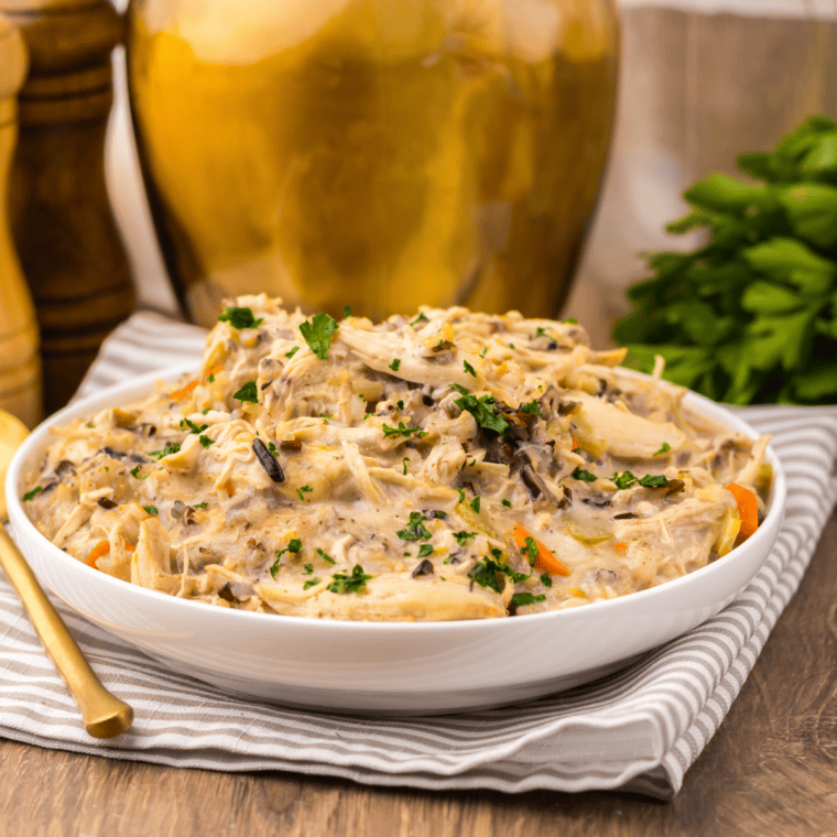 Bowl of creamy slow cooker chicken and wild rice soup with carrots and celery, garnished and served with crusty bread