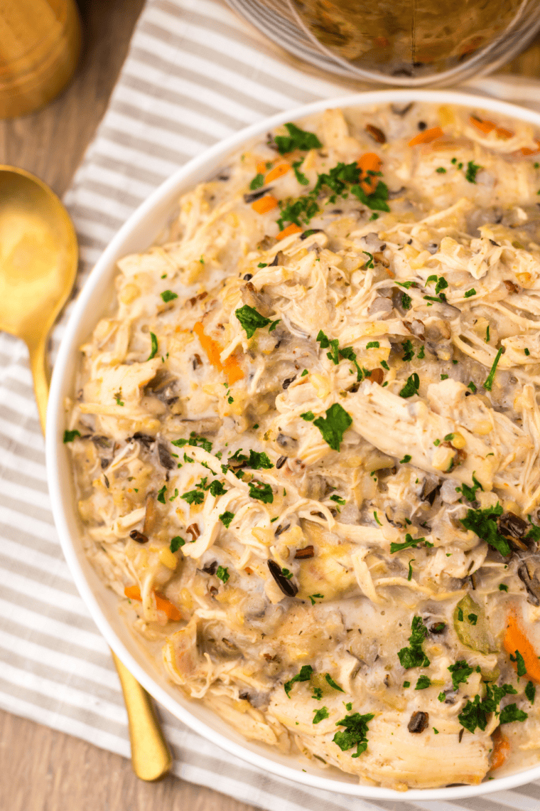 Bowl of creamy slow cooker chicken and wild rice soup with carrots and celery, served with crusty bread