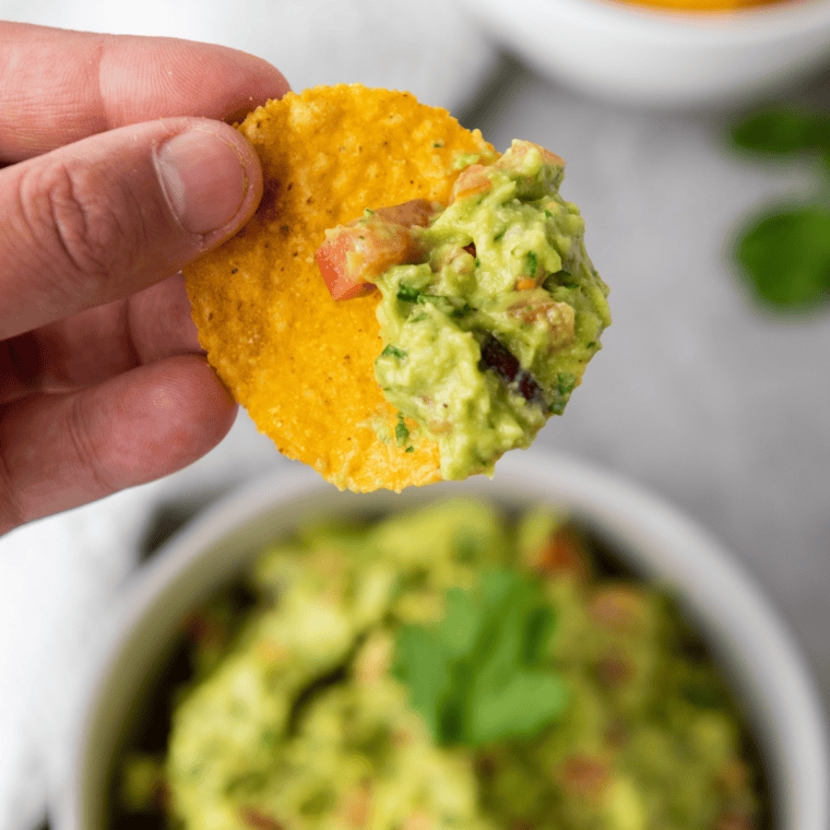 Spicy guacamole being mashed with a fork, cilantro and cured onion-chile mixture folded into the avocado