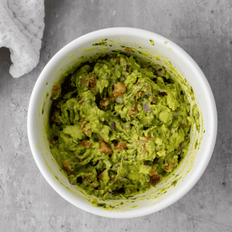 Ripe Hass avocado halved and crosshatched in the shell, flesh being scooped into a bowl with a spoon