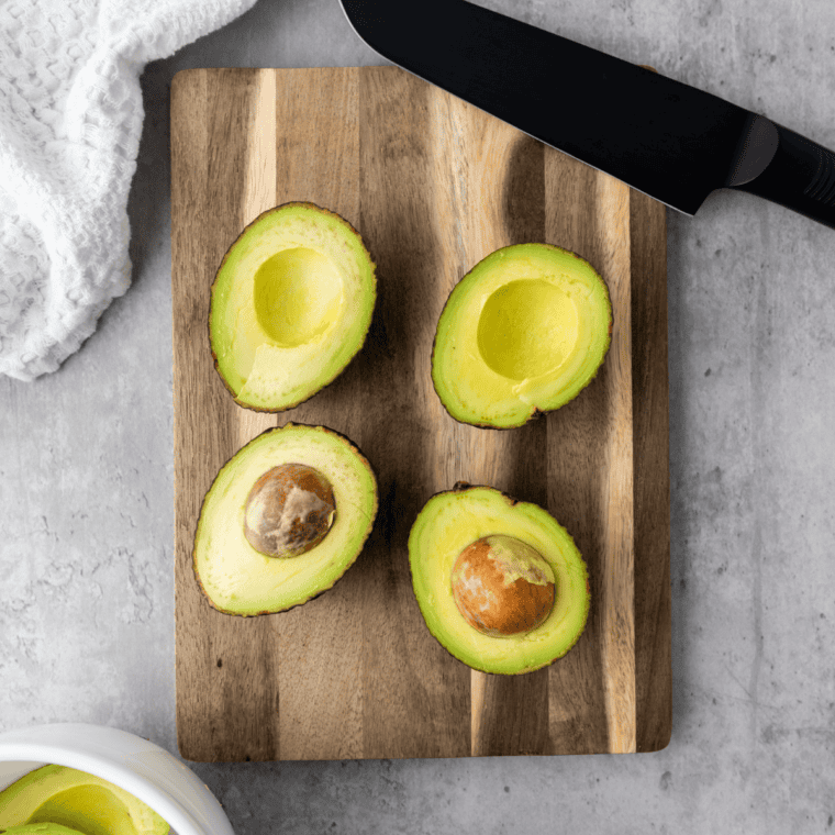 Halved avocados with the stone removed, flesh being scooped into a bowl with a spoon
