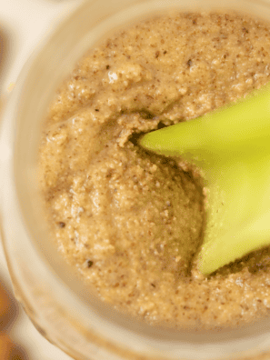 Celery stick scooping almond butter from a glass jar