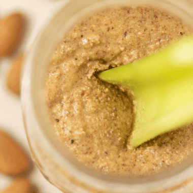 Celery stick scooping almond butter from a glass jar