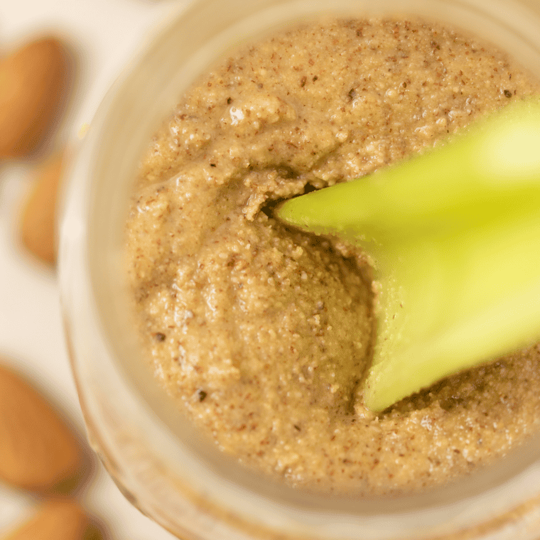 Celery stick scooping almond butter from a glass jar