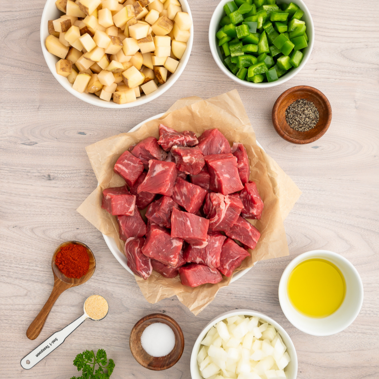 Ingredients for air fryer steak bites and potatoes including diced sirloin, potatoes, onion, bell pepper, olive oil, garlic powder, and smoked paprika