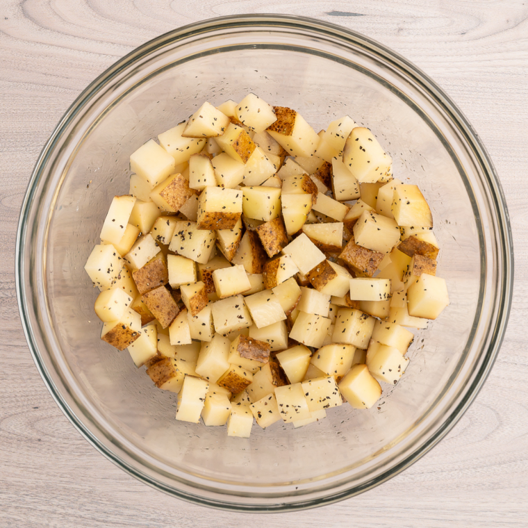 Diced potatoes tossed with olive oil, salt, and smoked paprika in a glass mixing bowl