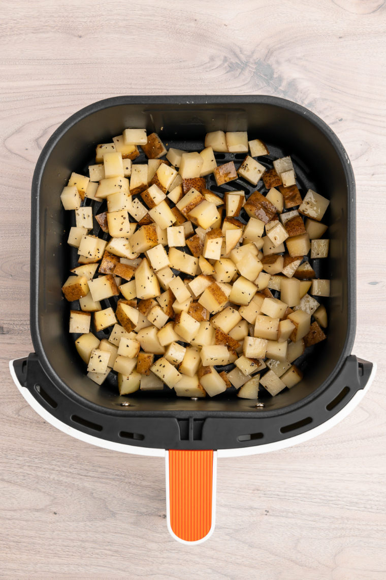 Seasoned diced potatoes arranged in a single layer in an air fryer basket