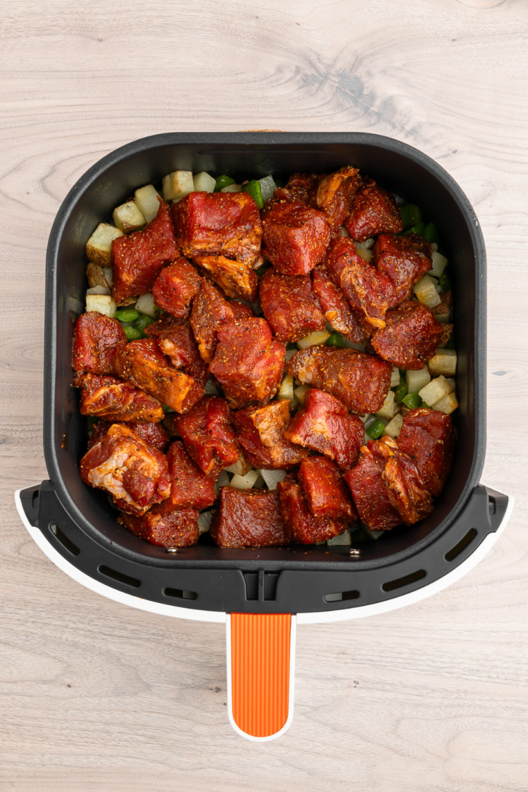 Seasoned sirloin steak bites, onions, and peppers added on top of crispy potatoes in the air fryer basket