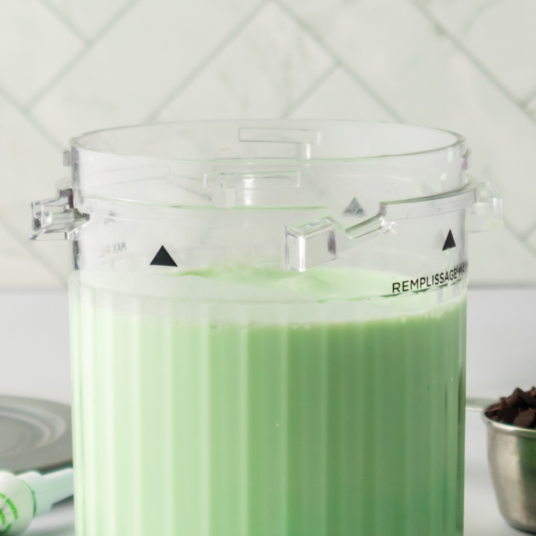 Bright green mint ice cream base poured into a Ninja Creami pint container, filled below the MAX line.