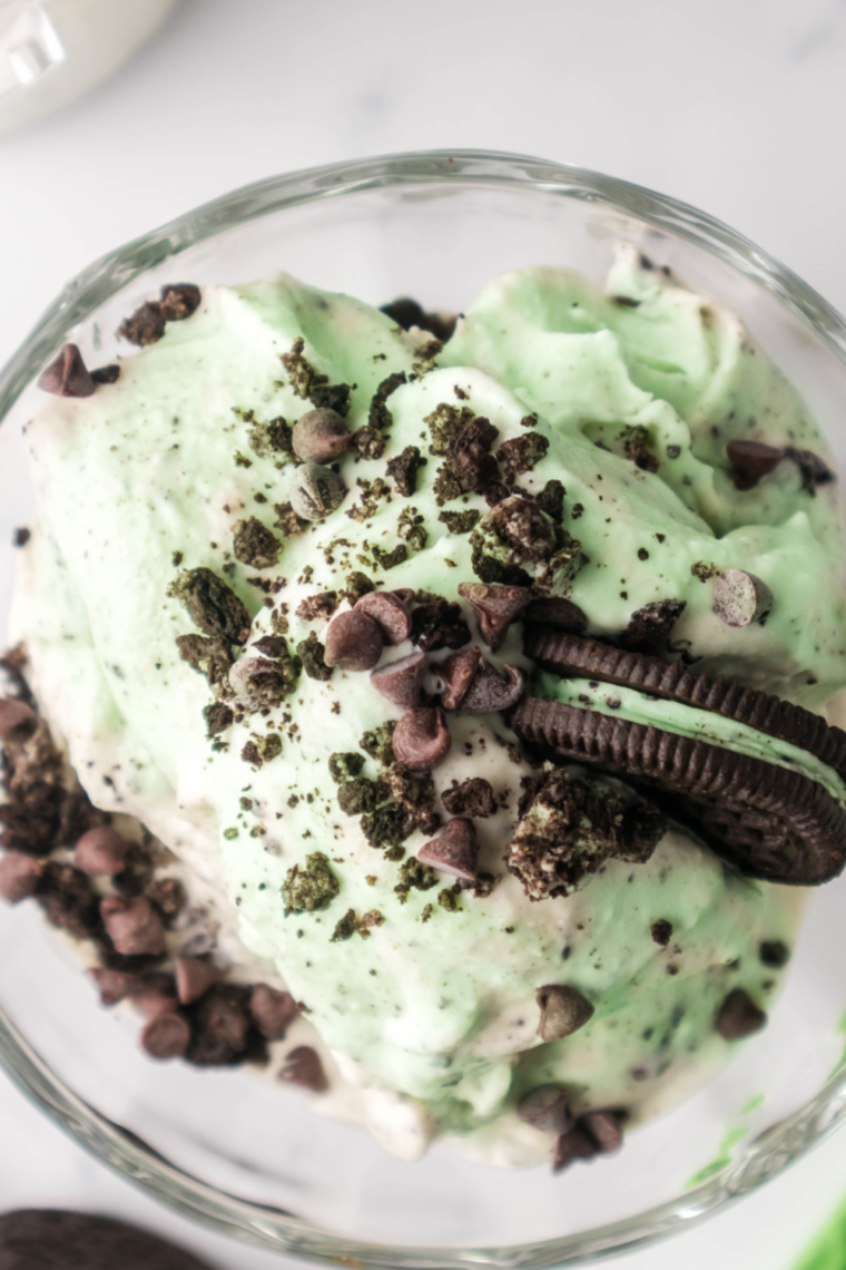 Scoops of copycat Blue Bell mint chocolate chip ice cream in a bowl, bright green with dark chocolate shards throughout.