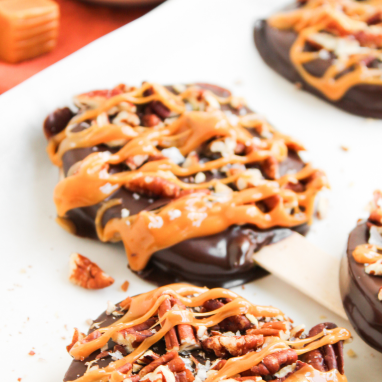 Caramel being drizzled over chocolate and pecan coated apple slices on sticks