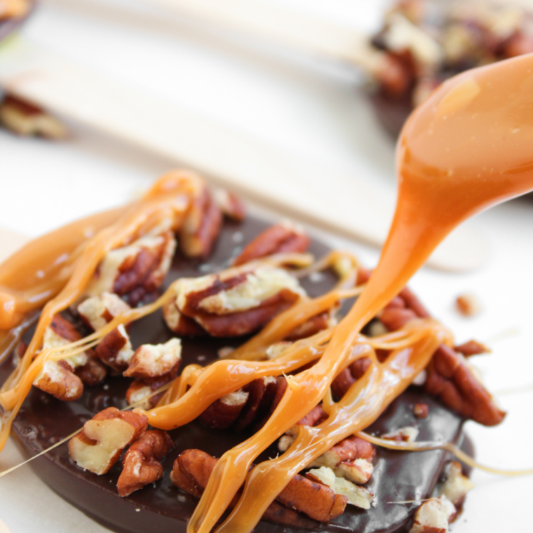 Three chocolate covered apple slices on sticks standing upright with caramel drizzle and sea salt