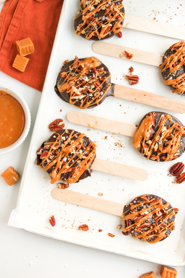 Chopped pecans being sprinkled over chocolate dipped apple slices on a parchment lined baking sheet