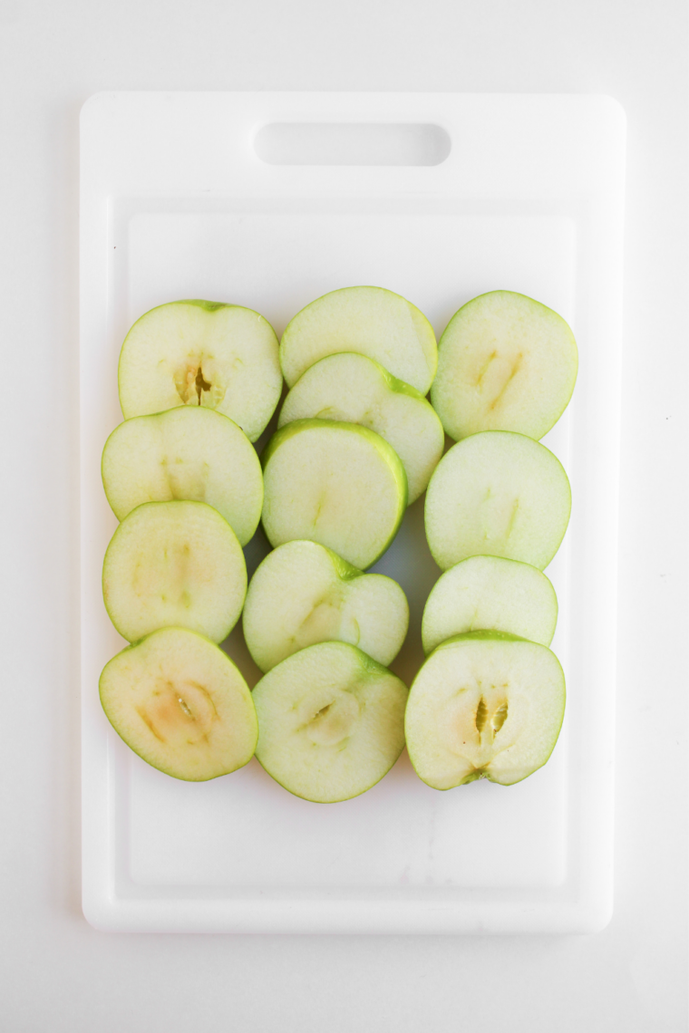 Three whole Granny Smith apples on a wooden cutting board before slicing