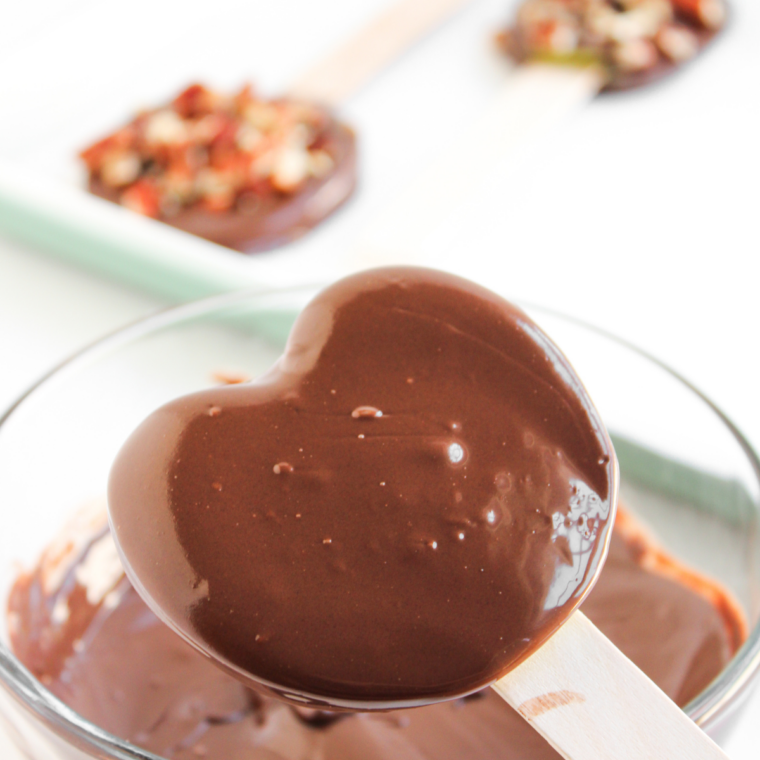 Hand dipping a Granny Smith apple slice into melted chocolate for caramel apple pops