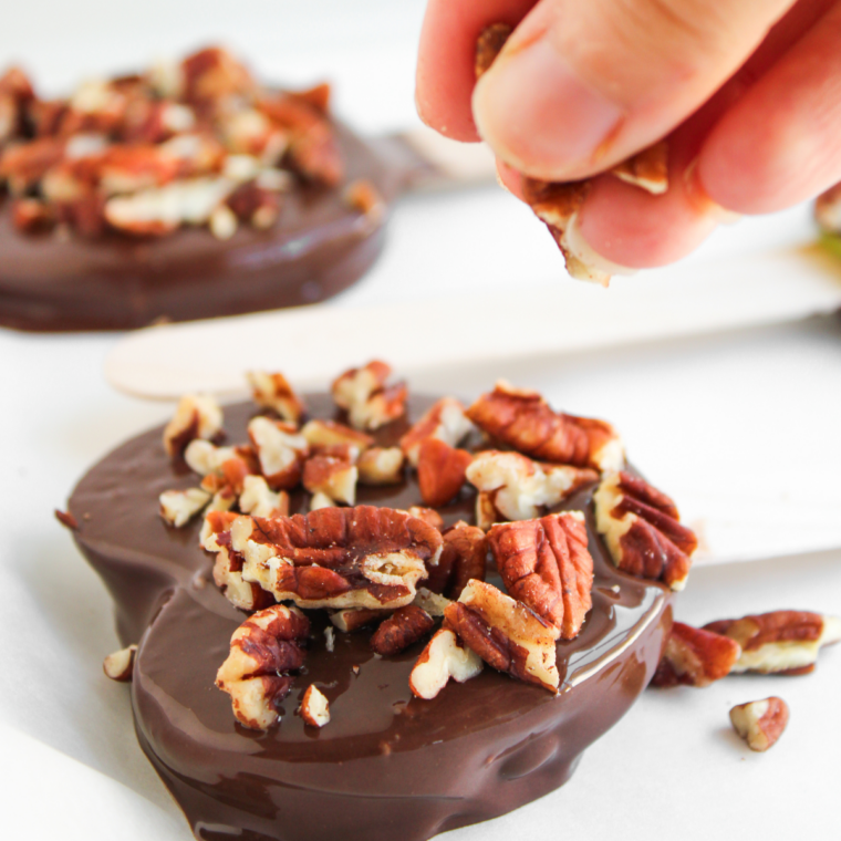 Chocolate coated apple slice held above a bowl while excess chocolate drips off