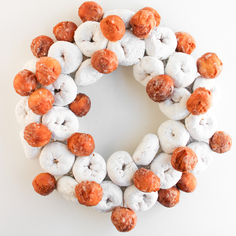 Glazed donut holes secured with toothpicks in the gaps between powdered mini donuts on a wreath