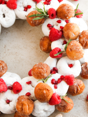 Christmas donut wreath made with powdered mini donuts, raspberries, pomegranate seeds, and fresh rosemary sprigs