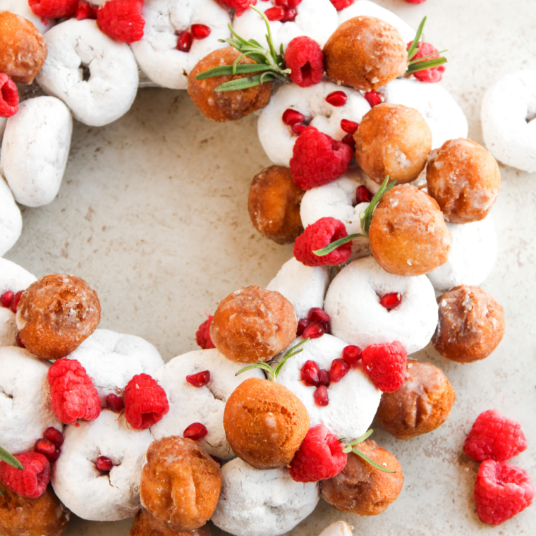 Christmas donut wreath made with powdered mini donuts, raspberries, pomegranate seeds, and fresh rosemary sprigs