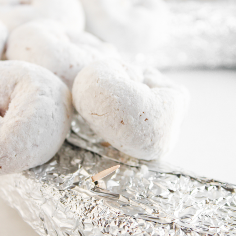 Pressing a powdered sugar mini donut onto a toothpick inserted at an angle in a foil-wrapped foam circle