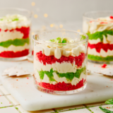 Red and green layered Christmas trifle dessert in a glass trifle bowl topped with whipped cream and cake crumbs