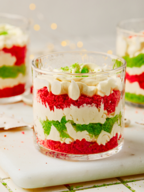Red and green layered Christmas trifle dessert in a glass trifle bowl topped with whipped cream and cake crumbs