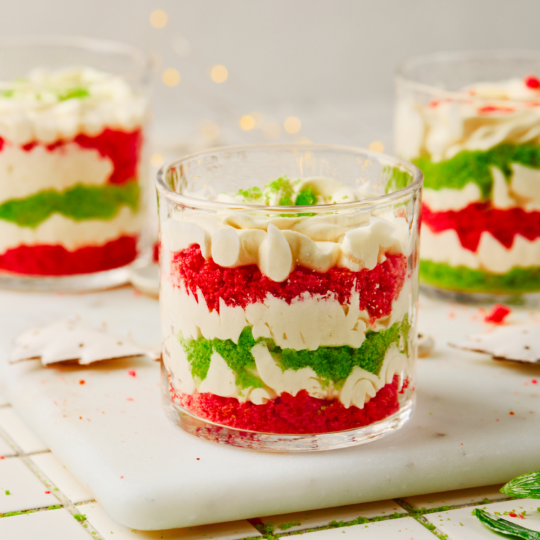 Red and green layered Christmas trifle dessert in a glass trifle bowl topped with whipped cream and cake crumbs