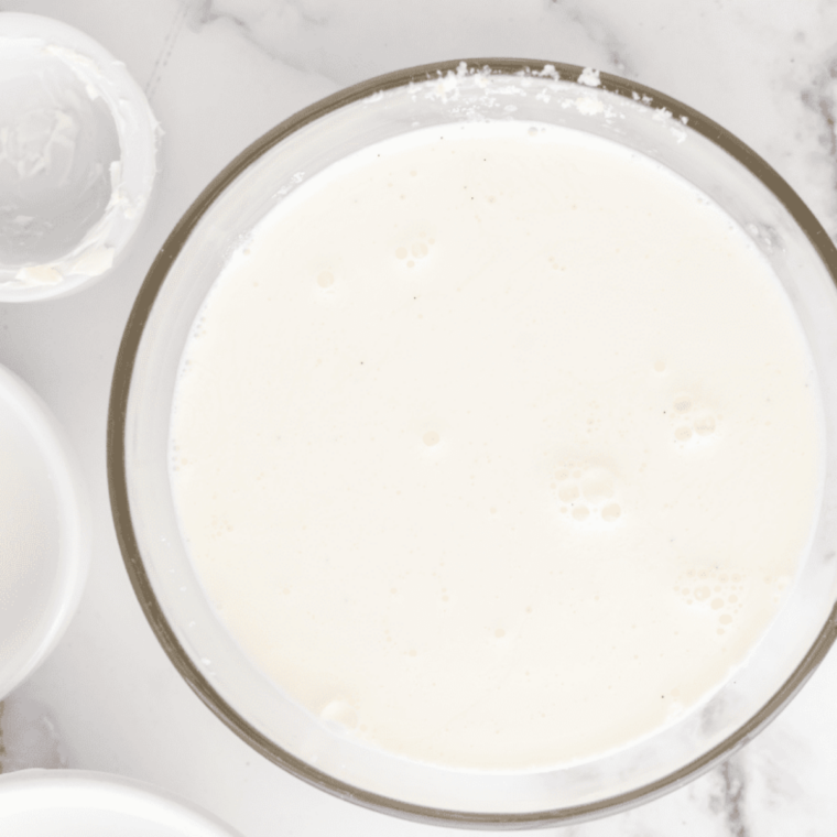 Adding milk, heavy cream, vanilla, and salt to the cream cheese base and whisking until fully dissolved and uniform
