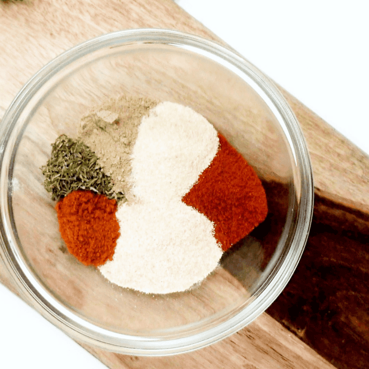 Cornstarch, paprika, thyme, onion powder and other spices in a white bowl before mixing into beef stew seasoning