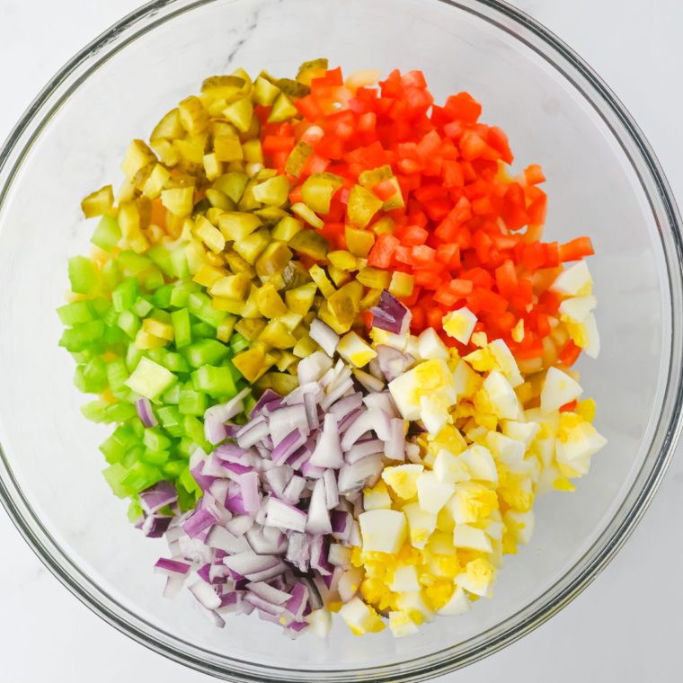Diced bell pepper, red onion, cucumber, and halved cherry tomatoes on a cutting board