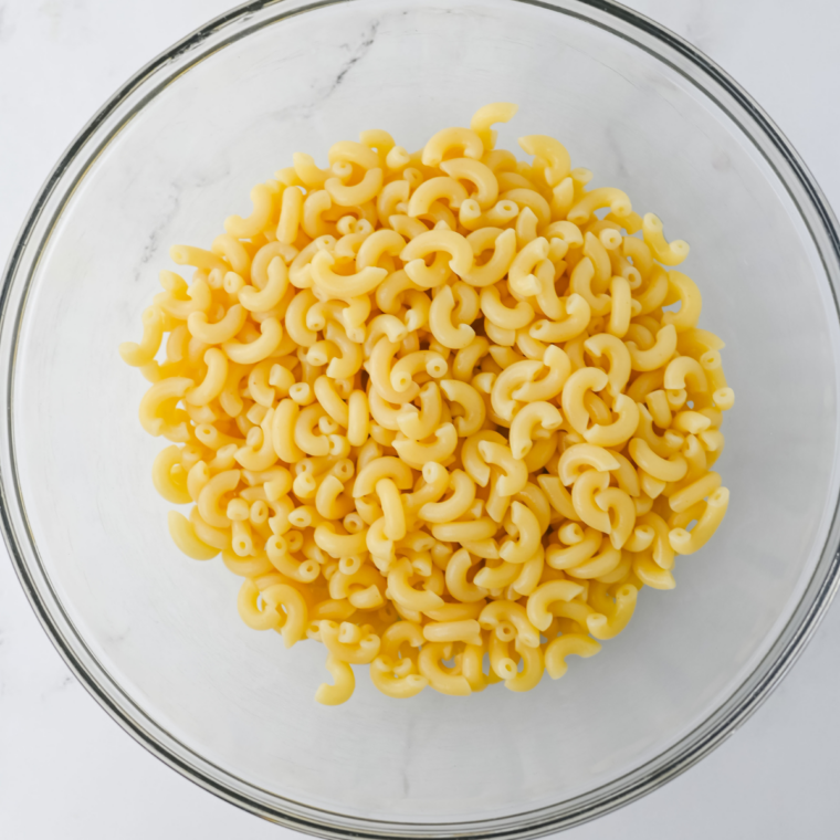 Cooked elbow macaroni cooling in a large white bowl before adding dressing