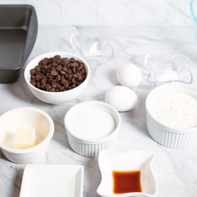 Ingredients for crock pot chocolate cobbler: flour, cocoa powder, brown sugar, butter, milk, and vanilla in glass bowls