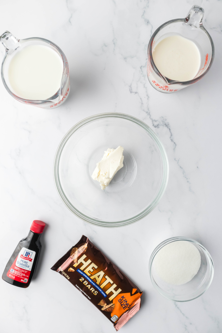 Ingredients for a healthy Ninja Creami Sonic Blast Reese's Cup laid out on a counter: chocolate protein powder, cocoa powder, powdered peanut butter, milk, Greek yogurt, and a Reese's cup