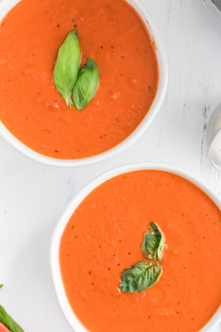 Overhead view of upgraded canned tomato soup in a shallow bowl with basil leaves and a swirl of cream on top.