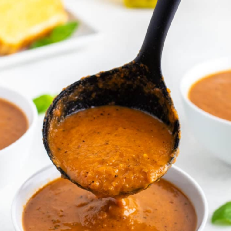 Half a grilled cheese sandwich being dipped into a bowl of creamy tomato soup.